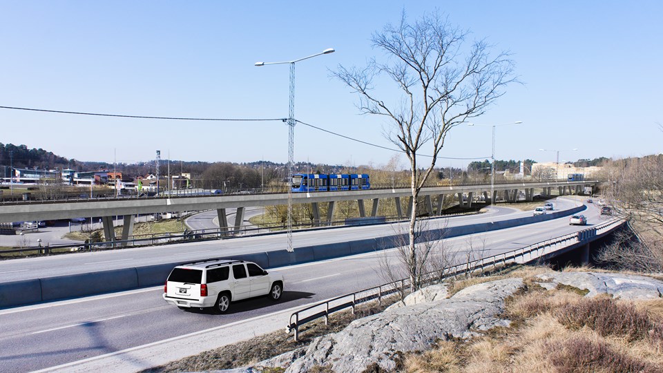 En bro för bilar och en bro för tvärbanan, över Bällstavägen. Bilar och tvärbanetåg syns på bilden och omgivningar med träd, vägar, hus. Foto