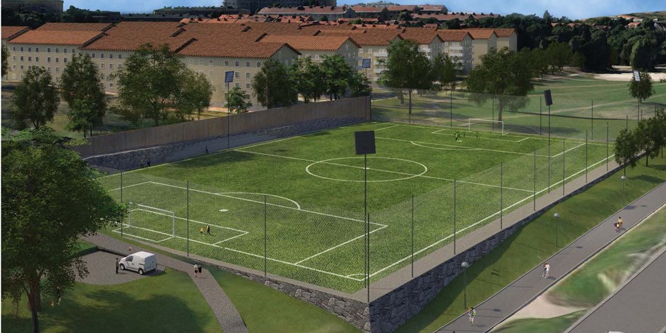 Fotbollsplan med stängsel runtom. Gångväg, bostadshus och träd som ligger i närheten. Illustration.