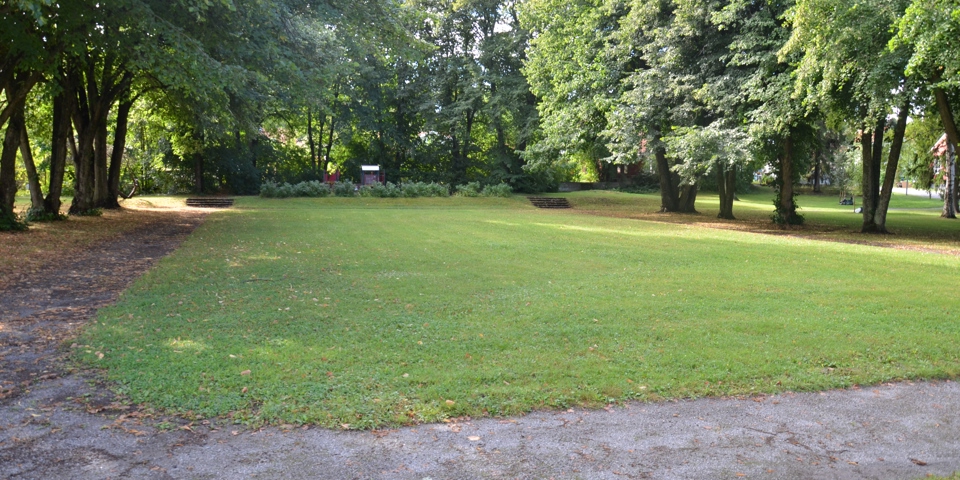 Parkmiljö med gräsmatta inbäddad av uppvuxna träd och gångbana. Foto