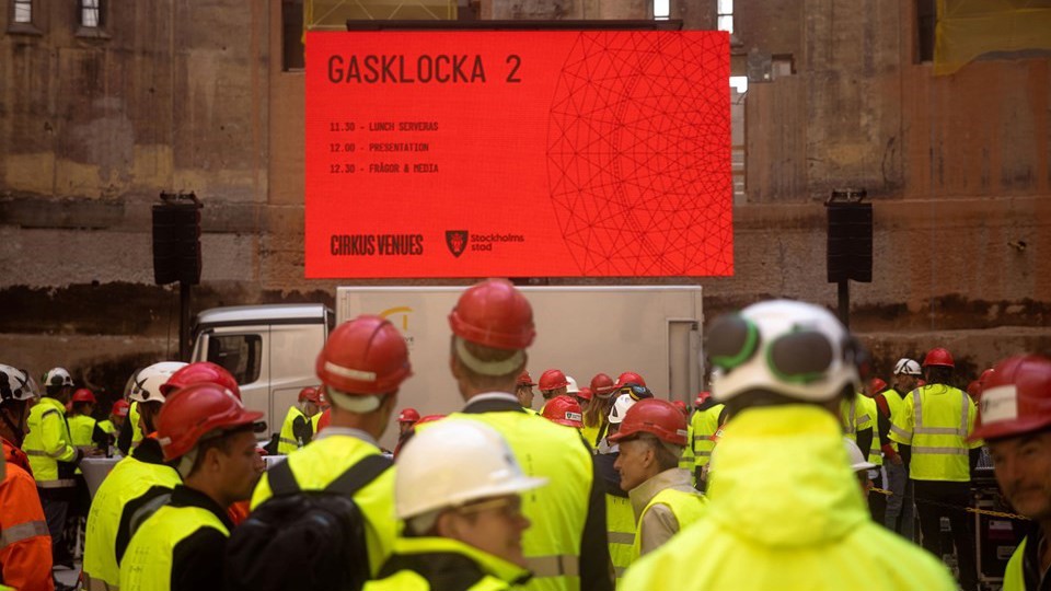Människor i gula jackor tittar mot en röd skärm. 