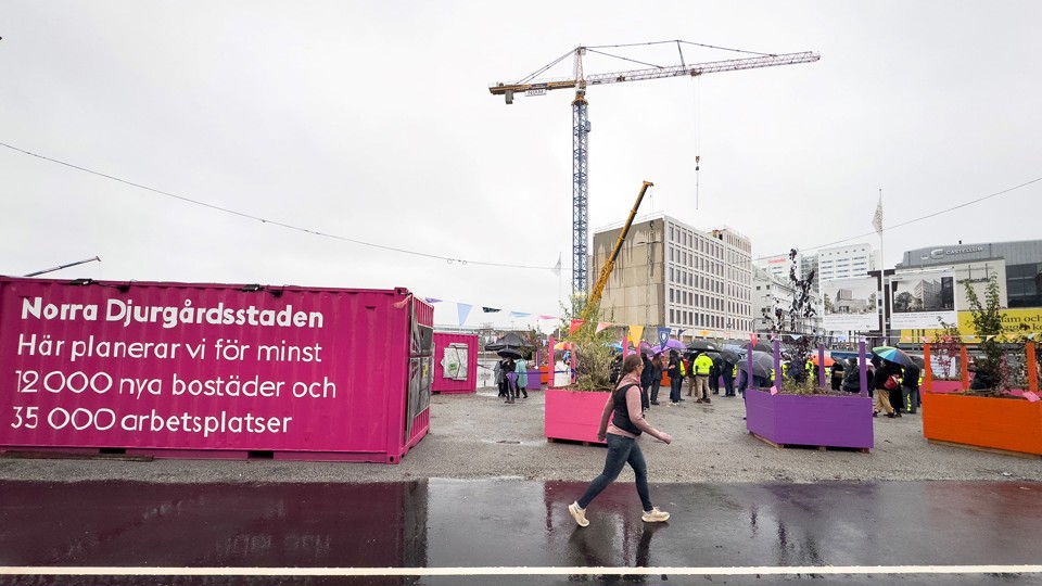 Rosa conteiner. Byggkran och människor på ett torg. 