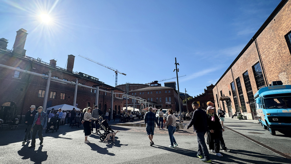Torg omringat av tegelbyggnader. Flera människor rör sig över torget. 