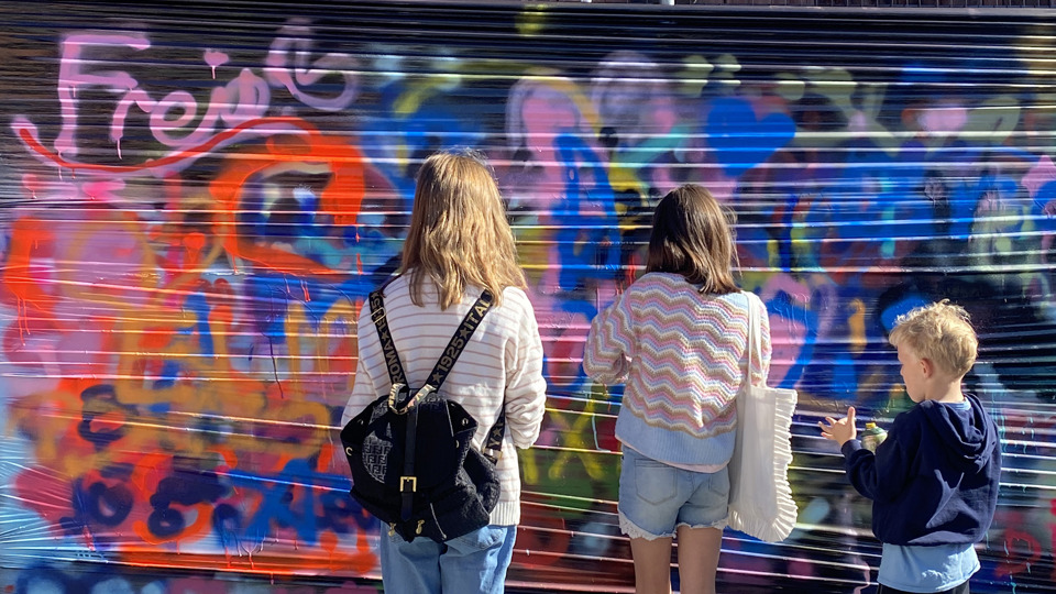 Tre barn som målar graffitti på en vägg. 