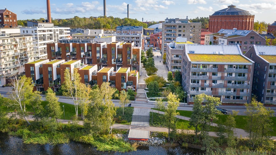 Flera flerbostadshus vid vatten. Grönska i förgrunden. 