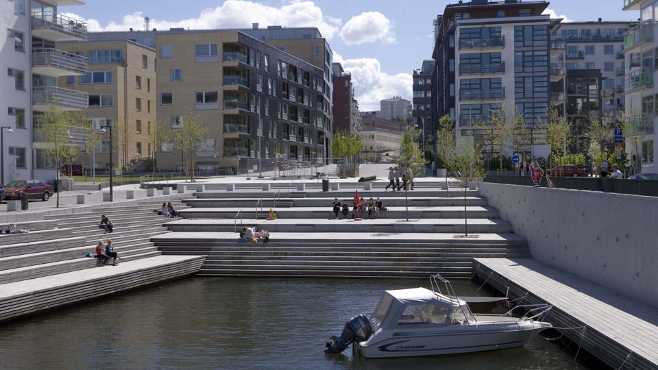 Trappa vid vatten, båtplatser, människor, i bakgrunden syns flerbostadshus, fotografi.