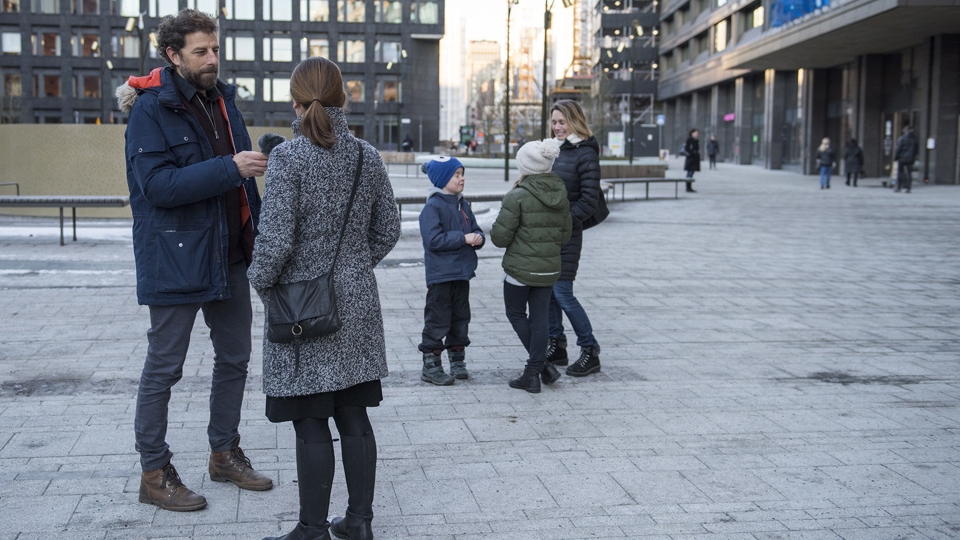 En man intervjuar en kvinna på ett torg. I bakgrunden syns en kvinna och två barn.