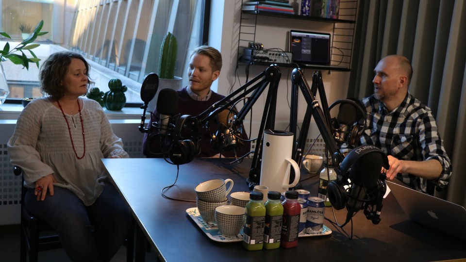 Poddinspelning med tre personer. Bricka med kaffe och juice i förgrunden.