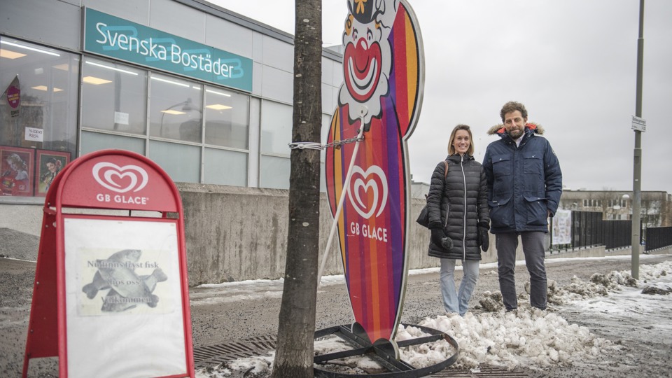 En kvinna och en man framför ett hus med skylten Svenska Bostäder. 