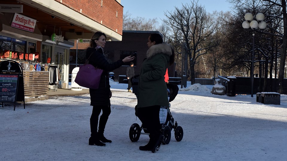 En kvinna intervjuar en kvinna med barnvagn på ett snöigt torg.