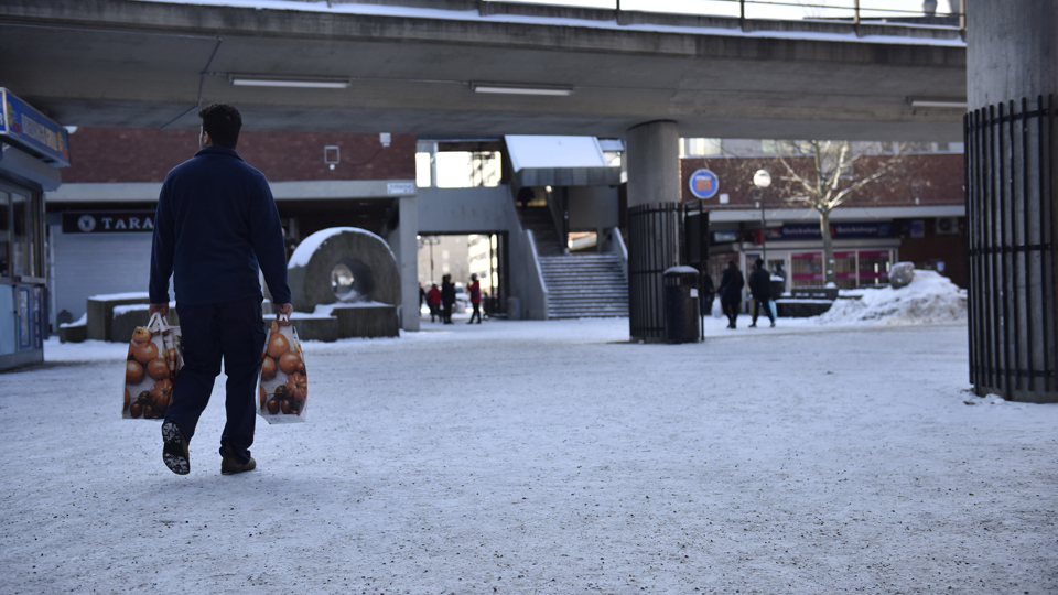 En person går över ett torg, under ett tunnelbanespår.