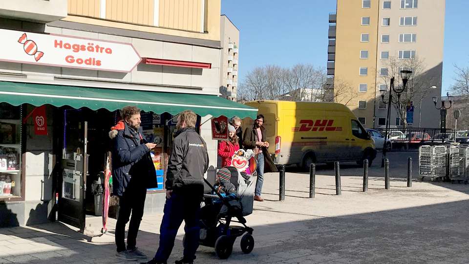 En man intervjuar en man med barnvagn på ett torg.