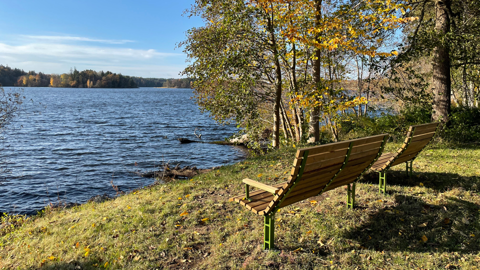 Två bänkar av trä som är placerade i strandkanten ut mot vattnet.