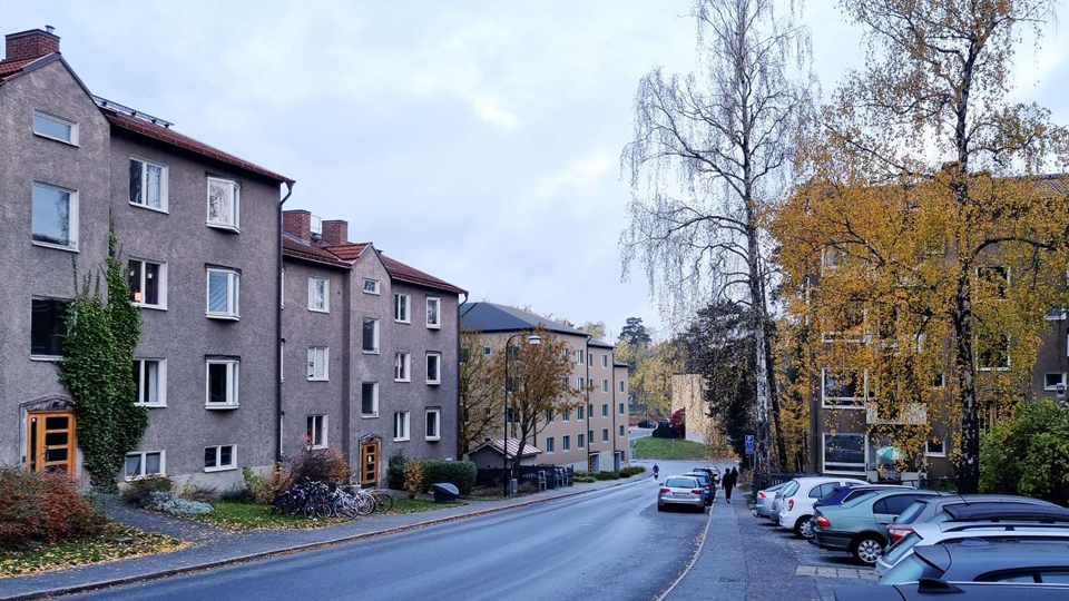 Flerbostadshus längs med gata, parkerade bilar, fotomontage.