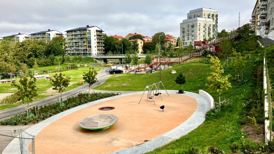 Lekplats i stort grönområde bredvid bostadshus, fotografi.