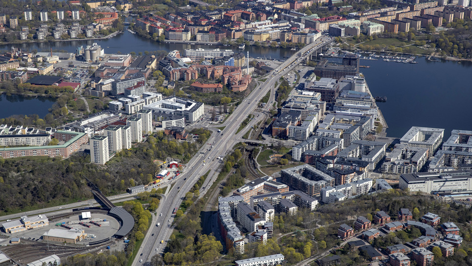 Flygvy över Liljeholmen med bostadshus och grönska, omgivet av vatten, foto.