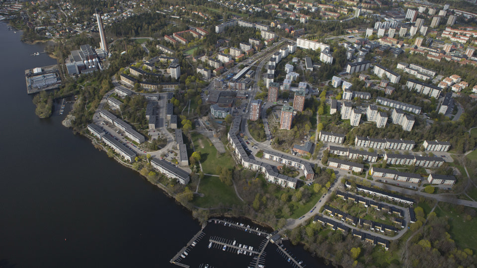 Flygvy över bostadsområde och värmeverk intill vatten, foto.