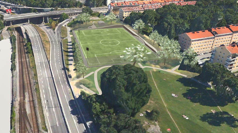 Fotbollsplan som ligger intill bilväg, tågspår, bostadshus, gräsmattor och träd. 3D-visualisering.