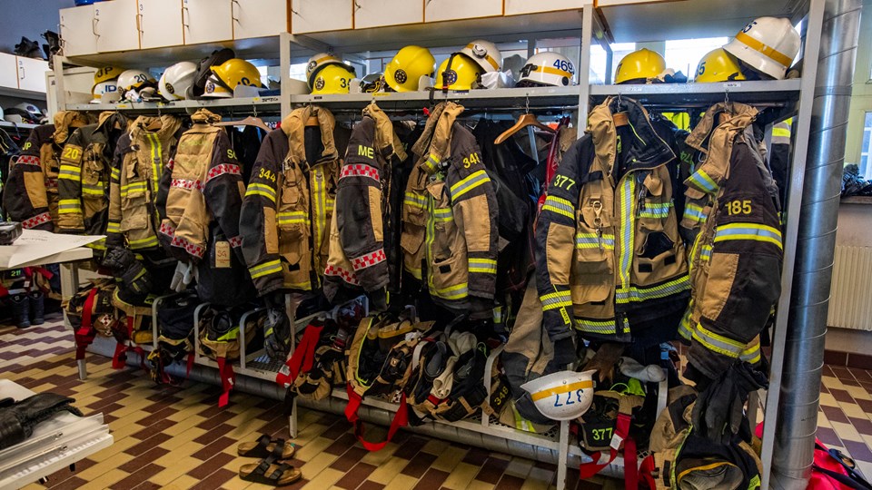 Brandmännens jackor byxor och hjälmar på en klädställning, foto. 