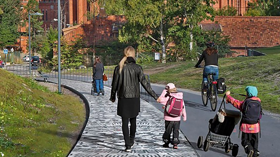 Barn och vuxna som går på gångväg. Cykelbana brevid där cyklist cyklar. Foto.