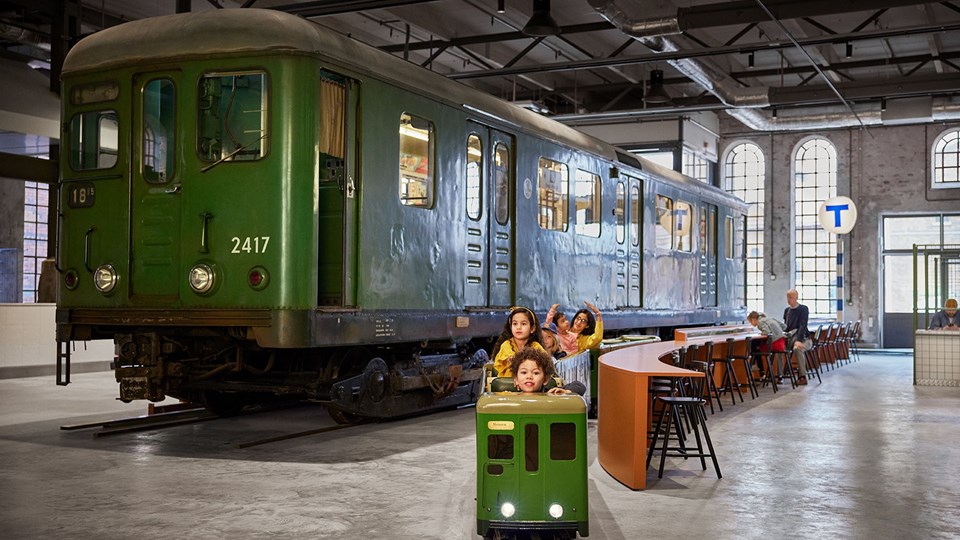 Grön tunnelbanevagn till vänster och barn som sitter i ett litet tåg bredvid. 