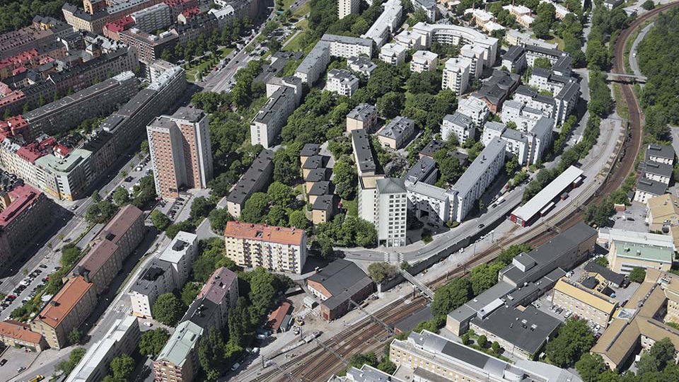 Flygfotografi över ett område med flerbostadshus och järnvägsspår.