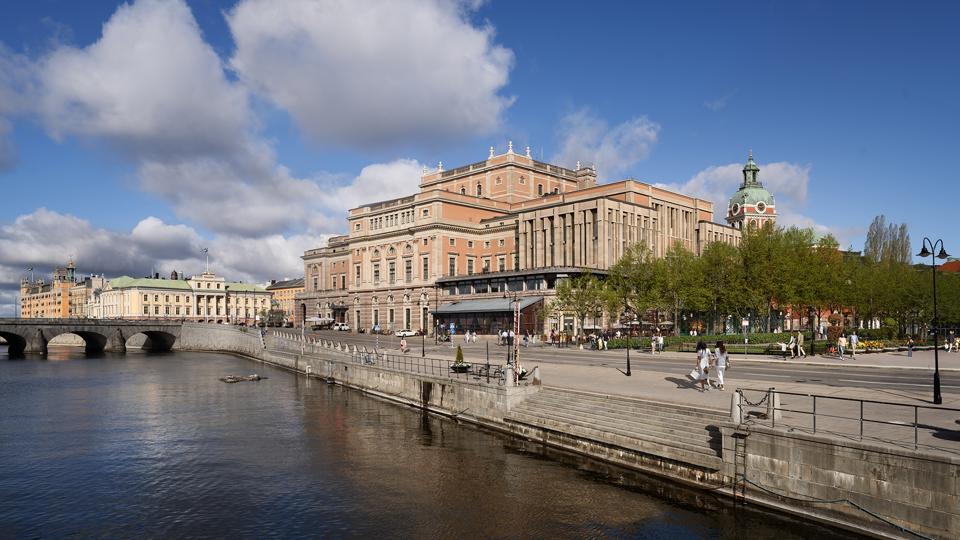 Visualisering av Kungliga Operan i Stockholm med en föreslagen påbyggnad, sett från Strömbron. Byggnaden och dess nya tillägg syns tydligt mot himlen.