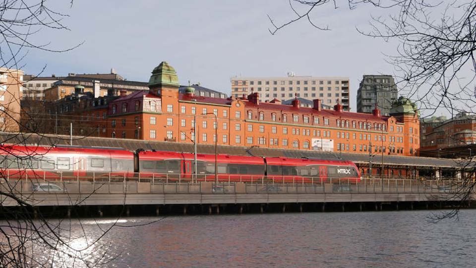 Vy mot tåg på spår, vatten, byggnader bakom, fotomontage.