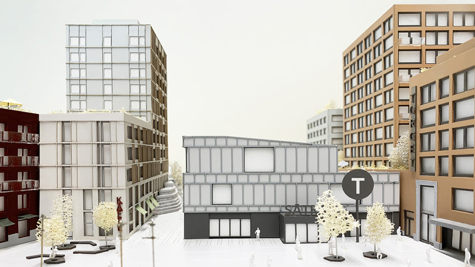  Torget vid Sätra Centrum och en grå  byggnad som är en biljetthall till tunnelbanan. Flerbostadshus omger biljetthallen. På torgets öppna yta syns planterade träd, sittplatser och människor i rörelse. Illustration