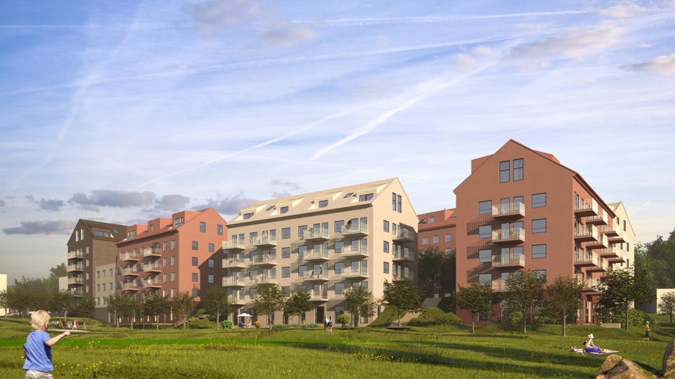 En grönskande äng med lekande barn. I bakgrunden syns bruna och röda bostadshus i flera våningar.
