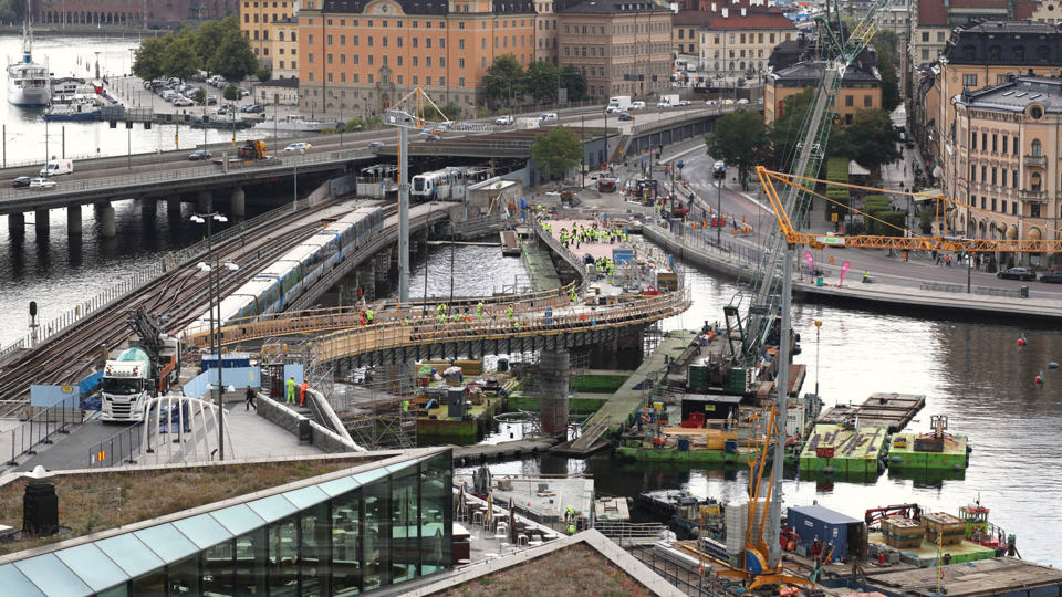 Översikt över bygget av en svängd bro över vattnet mellan Södermalm och Gamla stan.