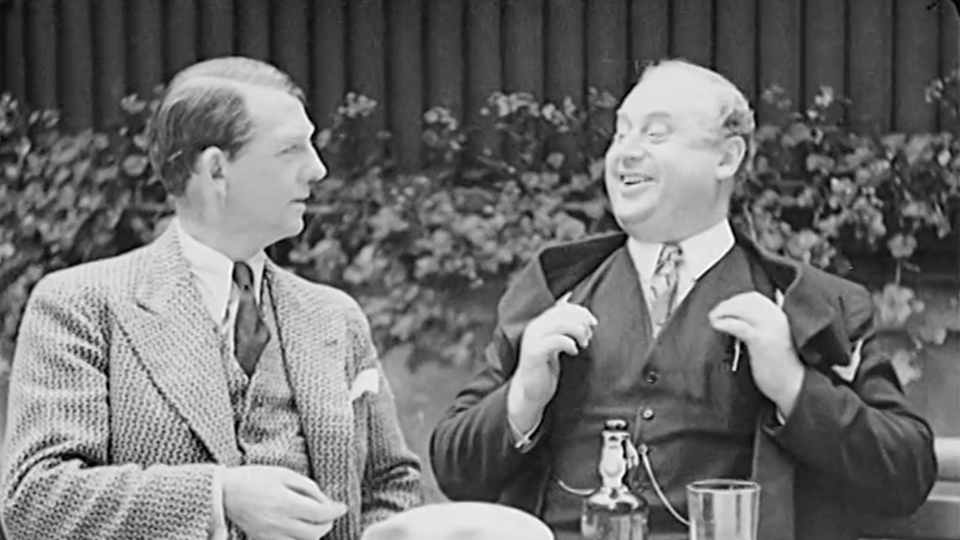 Svartvit bild från 1930-talet. Två män i kostym sitter vid ett bord.