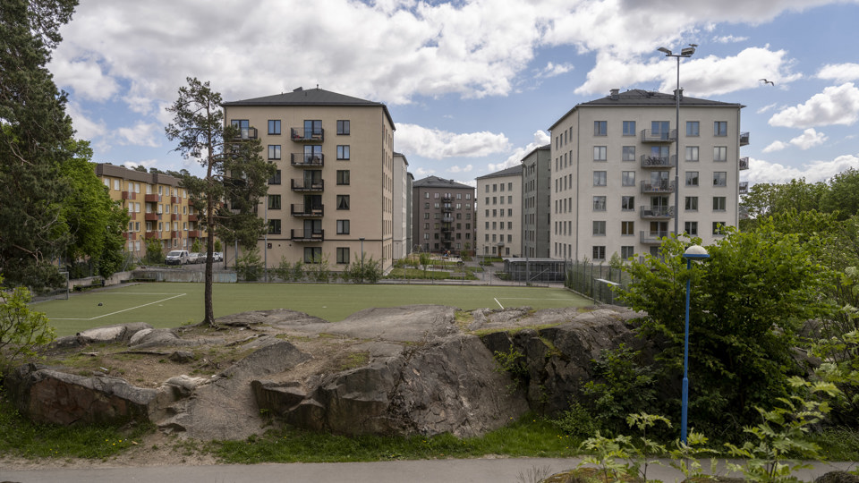 Ett antal flerstadsbohus i ljusa färger med en intilliggande fotbollsplan, foto.