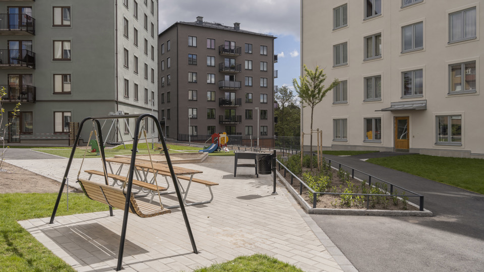 Innergård med hammock, bänkar och lekplats. Omgiven av flerbostadshus i grönt, brunt och beige, foto.