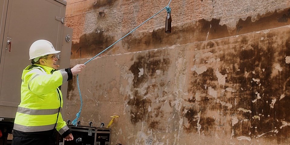 Kvinna i byggarbetskläder slänger glasflaska i en vägg. 