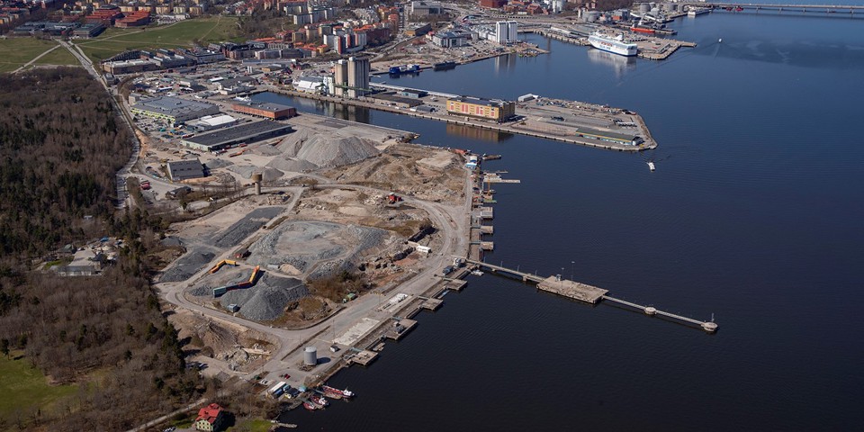Kustlinje med vatten till höger. Till vänster stora grushögar samt bebyggelse. 