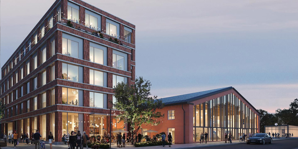 En modern byggnad med stora glasfönster och flera våningar, bredvid en renoverad industribyggnad, omgiven av människor som promenerar och sitter på en uteservering på kvällen.