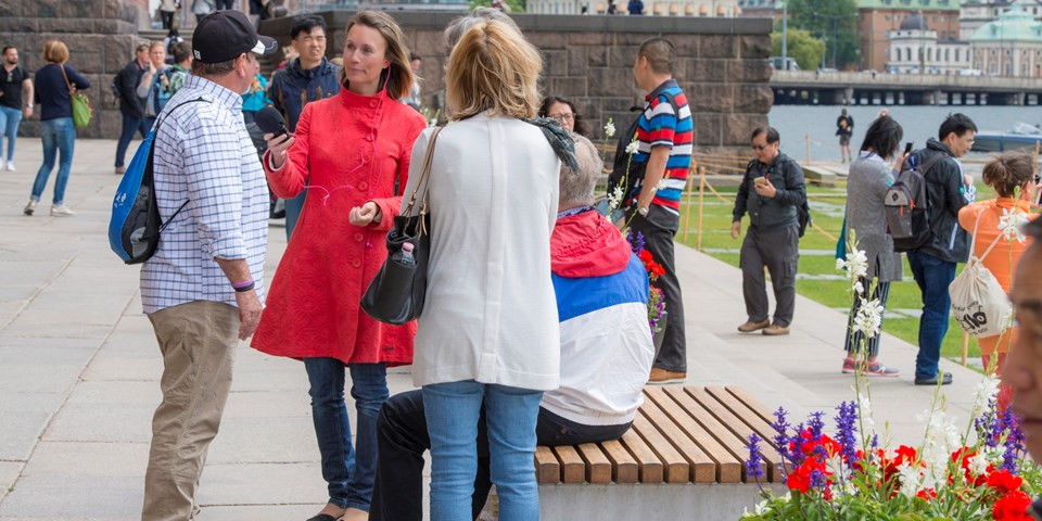 Kvinna i rött intervjuar man i keps utanför stadshuset.  Människor i bakgrunden.