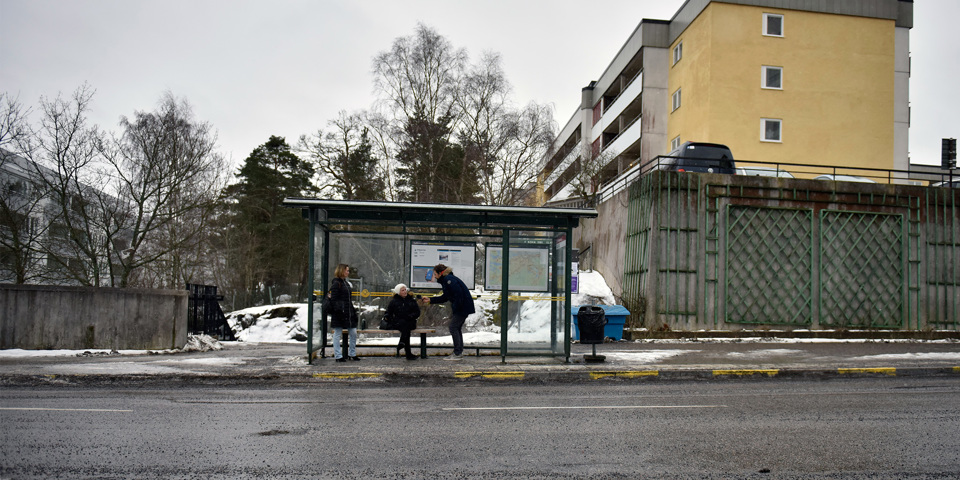 Kvinna intervjuas vid busshållsplats vid väg. Betong och snöslask i bakgrunden. 