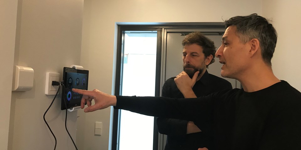Två män tittar på en digital skärm på väggen som är kopplad till en strömbrytare.
