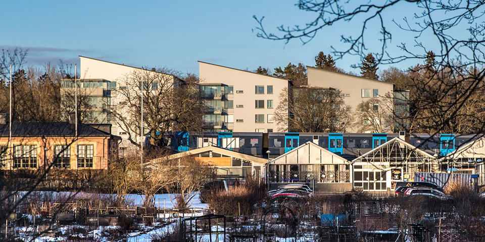 Kolonilotter, bostadshus, bilparkering och tunnelbana. Foto.