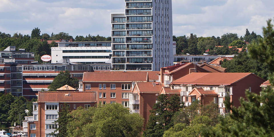 Bostadshus med flera våningar och stora balkonger samt kontorslokaler med omgivande träd och vatten. Foto.