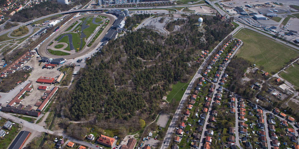 Flygvy över bostadshus, skogsområde, bilvägar och gräsytor, foto.
