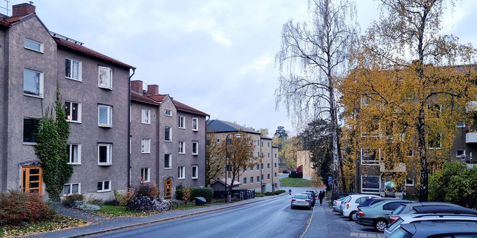 Flerbostadshus längs med gata, parkerade bilar, fotomontage.