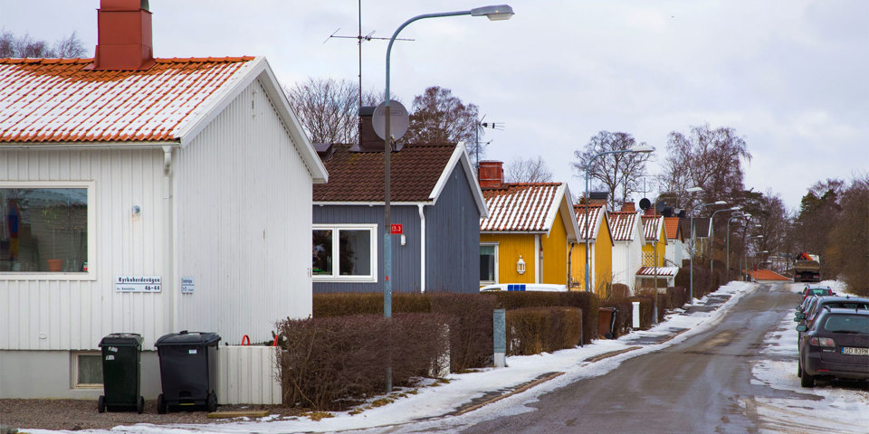 Småvillor i olika färger på rad på en gata, lite snö på marken, parkerade bilar, fotografi.