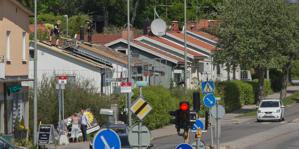 Gata i bostadsområde med trafikljus och vägskyltar. Gatan är  kantad av villor och träd, foto.