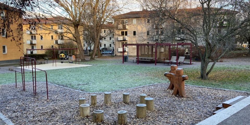 Lekplatsen Bomullen ligger i ett bostadsområde med gula och beigea flerfamiljshus. På lekplatsen finns en gräsmatta, flera träd och olika lekytor med gungor, små trädstubbar för de små barnen att sitta på och andra sittmöjligheter.