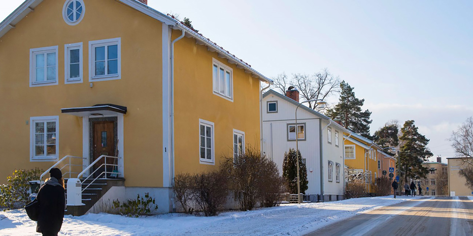 Villor vid bilväg. Människor som promenerar på trottoar. Foto.