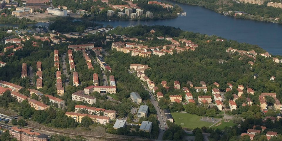 Bostadshus, skog, fotbollsplan och vatten. Foto.