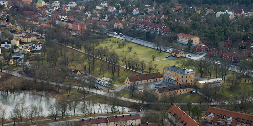 Ulvsunda slott som ligger vid vattnet. Bostadshus, stora gräsmattor och träd. Foto.
