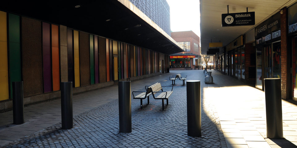 Pollare och sittbänkar vid gång i centrum med verksamheter längs med, fotografi.